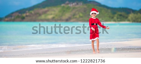 Adorable little girl in Santa hat and costume on tropical beach during Christmas holiday