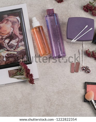 Moscow/Russia-CIRCA 11.2018: an image of beauty products of orange and purple colour bottles, eye shadows, blush,  sedum autumn fire flowers, cotton buds on a grey marble vanity table