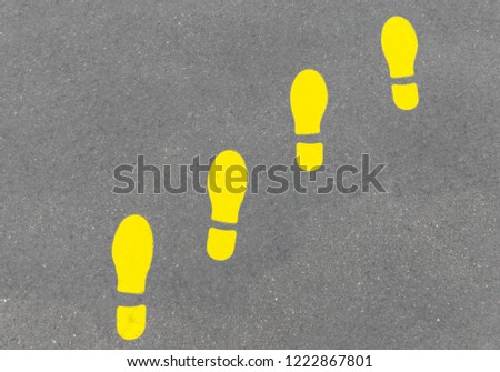 Yellow positive footprint or foot steps on gray asphalt. Horizontal shot.