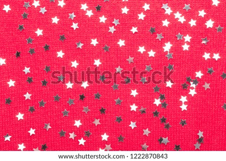 Silver star glitter on red knit background. Top view with copy space.