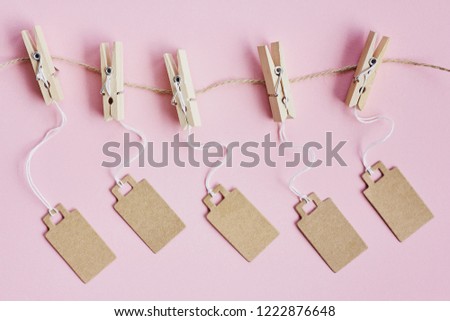Blank brown cardboard price tags, sale tag, gift tag, address label, luggage label hanging on clothes wooden clips on pink background. Mock up, copy space for text, top view