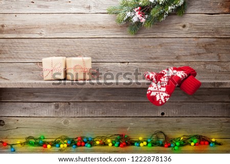 Christmas lights, gift boxes and mittens in front of wooden wall. With space for your greetings