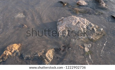 Sea shore with sand and stones and rocks in the water at sunset, close-up