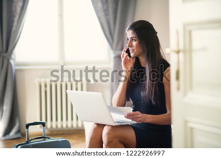 Young businesswoman on a business trip sitting in a hotel room, using laptop.
