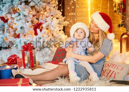 Mother with baby in a hat of Santa Claus in the Christmas room.