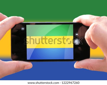 The concept of tourism and travel. The hands of men make a telephone photograph of the flag of Gabon. On the smartphone close-up image of the flag. Photos for social networks, blogs, instagram.