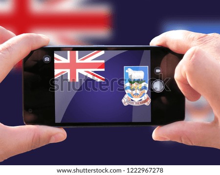 The concept of tourism and travel. The hands of men make a telephone photograph of the flag of Falkland Islands. On the smartphone close-up image of the flag. Photos for social networks, blogs