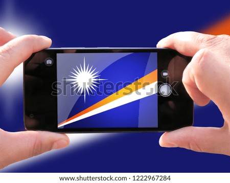 The concept of tourism and travel. The hands of men make a telephone photograph of the flag of Marshall Islands. On the smartphone closeup image of the flag. Photos for social networks, blogs