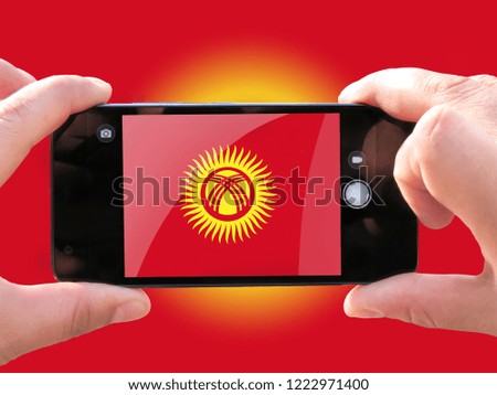 The concept of tourism and travel. The hands of men make a telephone photograph of the flag of Kyrgyzstan. On the smartphone close-up image of the flag. Photos for social networks, blogs, instagram.
