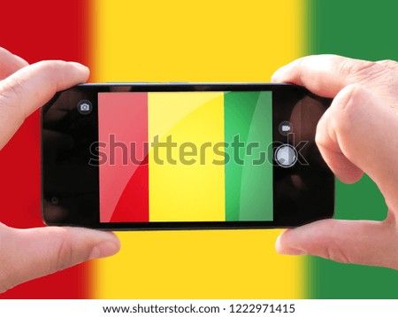 The concept of tourism and travel. The hands of men make a telephone photograph of the flag of Guinea. On the smartphone close-up image of the flag. Photos for social networks, blogs, instagram.