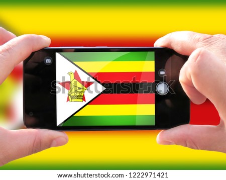 The concept of tourism and travel. The hands of men make a telephone photograph of the flag of Zimbabwe. On the smartphone close-up image of the flag. Photos for social networks, blogs, instagram.