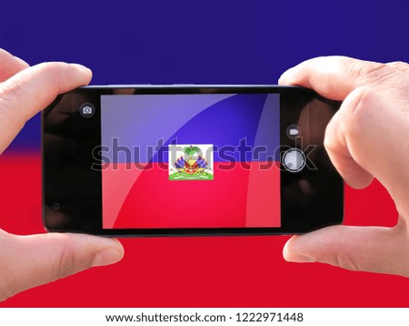 The concept of tourism and travel. The hands of men make a telephone photograph of the flag of Haiti. On the smartphone close-up image of the flag. Photos for social networks, blogs, instagram.