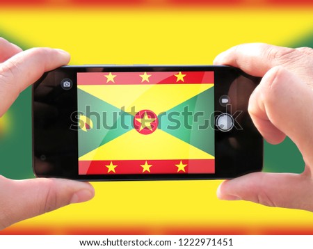 The concept of tourism and travel. The hands of men make a telephone photograph of the flag of Grenada. On the smartphone close-up image of the flag. Photos for social networks, blogs, instagram.