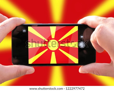 The concept of tourism and travel. The hands of men make a telephone photograph of the flag of Macedonia. On the smartphone close-up image of the flag. Photos for social networks, blogs, instagram.
