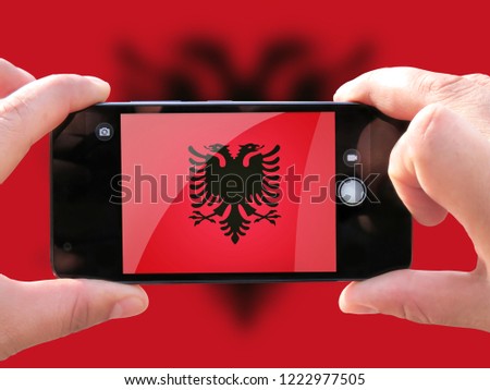 The concept of tourism and travel. The hands of men make a telephone photograph of the flag of Albania. On the smartphone close-up image of the flag. Photos for social networks, blogs, instagram.