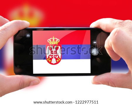 The concept of tourism and travel. The hands of men make a telephone photograph of the flag of Serbia. On the smartphone close-up image of the flag. Photos for social networks, blogs, instagram.