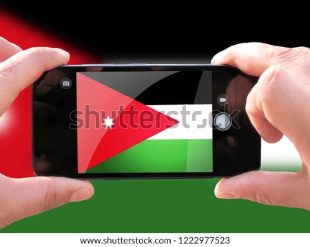 The concept of tourism and travel. The hands of men make a telephone photograph of the flag of Jordan. On the smartphone close-up image of the flag. Photos for social networks, blogs, instagram.
