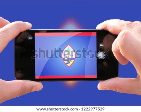 The concept of tourism and travel. The hands of men make a telephone photograph of the flag of Guam. On the smartphone close-up image of the flag. Photos for social networks, blogs, instagram.