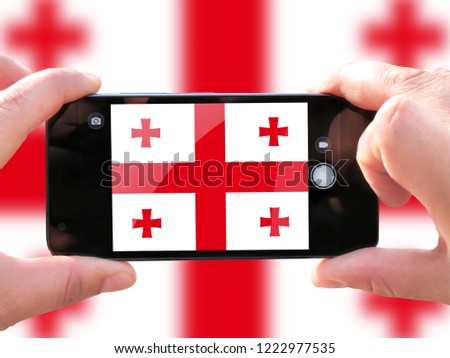 The concept of tourism and travel. The hands of men make a telephone photograph of the flag of Georgia. On the smartphone close-up image of the flag. Photos for social networks, blogs, instagram.