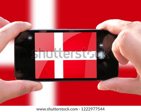 The concept of tourism and travel. The hands of men make a telephone photograph of the flag of Denmark. On the smartphone close-up image of the flag. Photos for social networks, blogs, instagram.