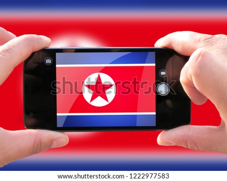 The concept of tourism and travel. The hands of men make a telephone photograph of the flag of North Korea. On the smartphone close-up image of the flag. Photos for social networks, blogs, instagram.
