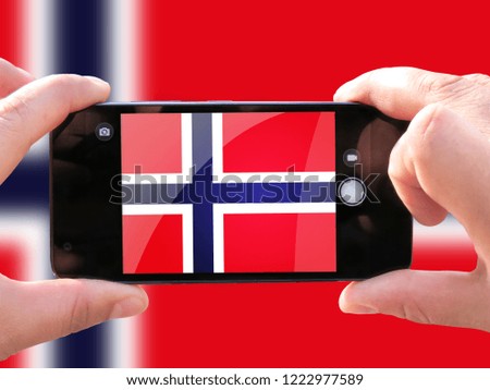 The concept of tourism and travel. The hands of men make a telephone photograph of the flag of Norway. On the smartphone close-up image of the flag. Photos for social networks, blogs, instagram.