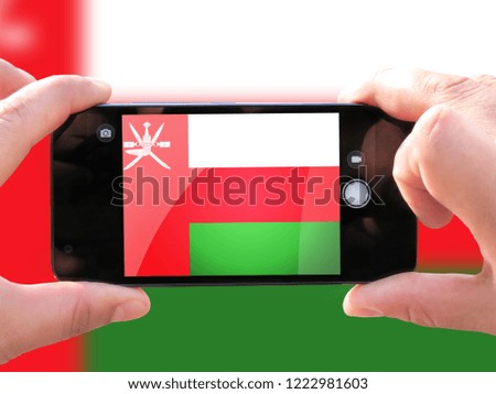 The concept of tourism and travel. The hands of men make a telephone photograph of the flag of Oman. On the smartphone close-up image of the flag. Photos for social networks, blogs, instagram.