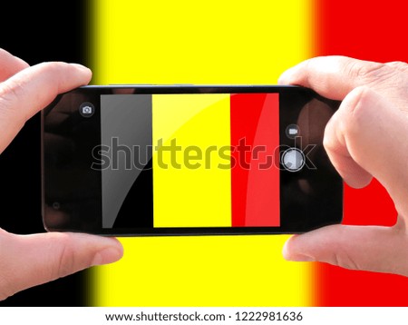 The concept of tourism and travel. The hands of men make a telephone photograph of the flag of Belgium. On the smartphone close-up image of the flag. Photos for social networks, blogs, instagram.