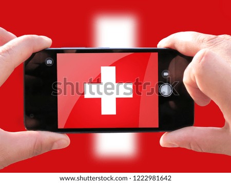 The concept of tourism and travel. The hands of men make a telephone photograph of the flag of Switzerland. On the smartphone close-up image of the flag. Photos for social networks, blogs, instagram.