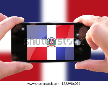 The concept of tourism and travel. The hands of men make a telephone photograph of the flag of Dominican Republic. On the smartphone close-up image of the flag. Photos for social networks, blogs