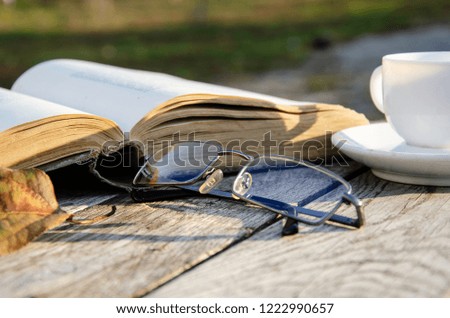 Book, cup of coffee on a wooden table in the autumn garden.
