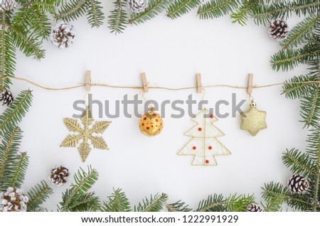Christmas frame made of christmas tree fir branches. Oon the rope with clothespins hanging toys, a star, New Year's toys, gold decorations, gifts on white background. Christmas greeting card flat lay