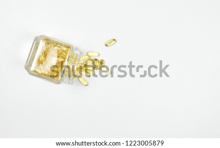 Top view of Pile overflow of fish oil capsules isolated in a glass bottle on white background. Omega 3. Vitamin E. Supplementary food background. Salmon capsules view. Copy space.