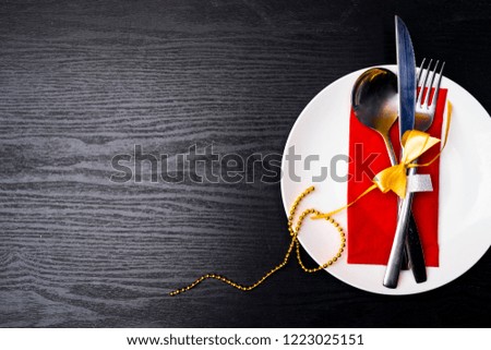 Christmas table setting with festive decorations on red napkin over wooden black background with copy space.