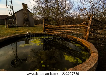 Sunrise at Rundown Ranch House with  stagnant water tank in foreground and windmill reflection.