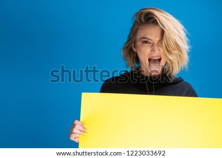 Funny dark blonde pulling hertongue out while holding an advertising cardboard and maing funny faces. Copy space available for ads