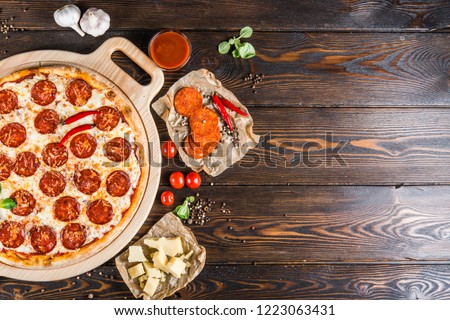 Food background design. Pizza with salami and pepperoni sausage on a round cutting board on a dark wooden background. Pizza Ingredients. Top view Royalty-Free Stock Photo #1223063431