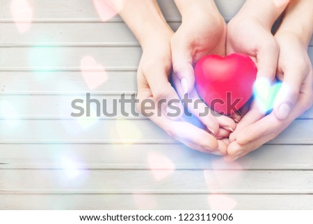 Mom Mother's hand holding daughter, son child kid palm supporting red heart love ball on light white wood background: Nursing children home day care health care concept: Hospital medical business Royalty-Free Stock Photo #1223119006