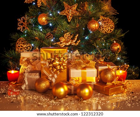 Picture of many golden presents boxes under luxury Christmas tree, beautiful adorned New Year spruce, shiny xmas decoration, holiday gifts, Christmastime party, festive ornament, yellow candle light