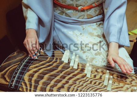 A woman wearing kimono is playing Koto - a traditional Japanese stringed musical instrument