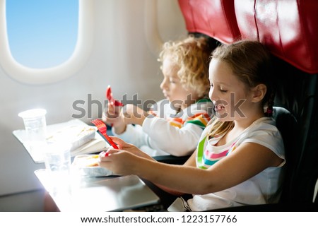 Child in airplane window seat. Kids flight meal. Children fly. Special inflight menu, food and drink for baby and kid. Girl and boy eating healthy lunch in airplane. Travel and family vacation.   Royalty-Free Stock Photo #1223157766