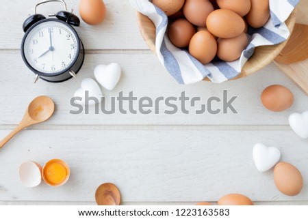 copy space frame for text on white kitchen table with fresh raw eggs, yellow yolk eggs, white heart shape sign and classic vintage clock.