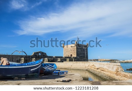 A view of a fisherman and blue boats with citadel in the background. Skala de la Ville, Essaouira, Morocco.