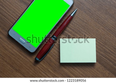 smartphone with green background, sticky note and red pen on wood background.