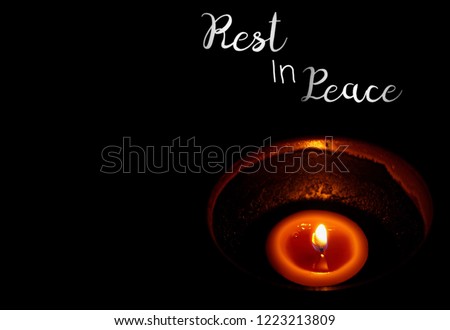 Yellow light candle in modern cup and word "Rest in Peace" isolated on black background. End of life. Sadness. Copy space for any text design. Royalty-Free Stock Photo #1223213809