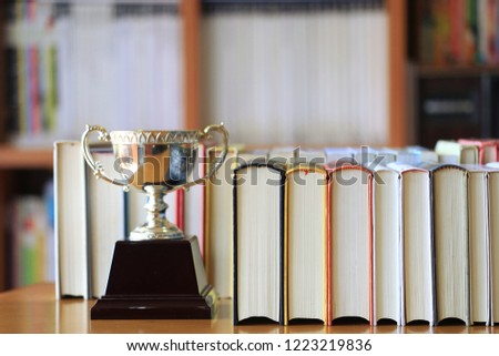 Close-up of multi-colored books placed lined up on a table in a library. Trophies placed near bookshelf is the background.selective focus and shallow depth of field