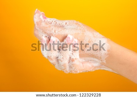 Woman's hands in soapsuds, on orange background close-up