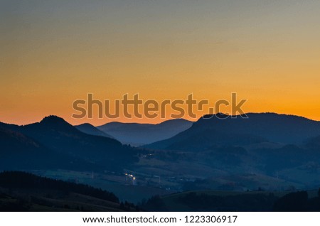 Colourful sunset above the mountain range. Light trails from cars moving on a mountain road. 
