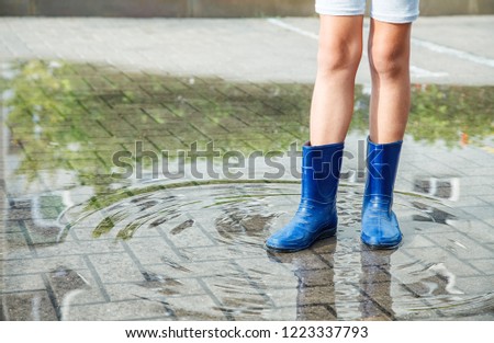 girl in rubber boots standing in a puddle after a rain outdoor on summer day. legs closeup