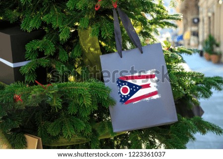 Ohio state flag printed on a Christmas gift box. Printed present box decorations on a Xmas tree branch on a street. Christmas shopping in United States, local market sale and deals concept. 